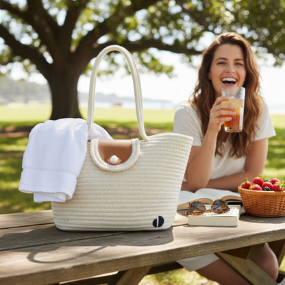 Woman enjoying a drink outdoors with a white woven tote bag on a wooden table. - dotflakes