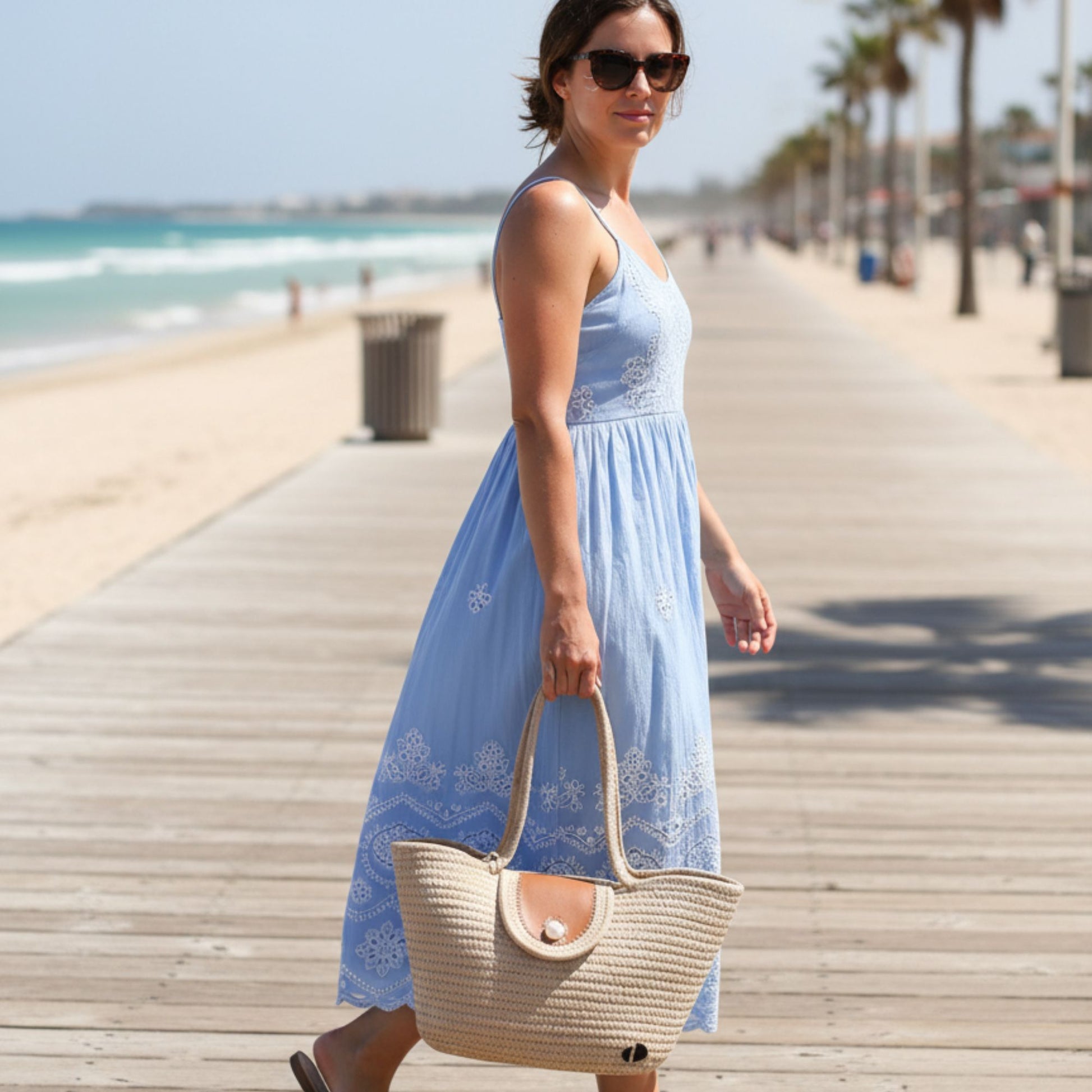 Woman in a blue dress holding a tote bag on a beach boardwalk. - dotflakes